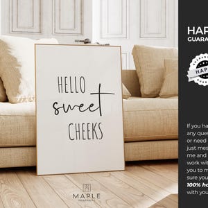 May include: A framed white print with the words "HELLO sweet CHEEKS" in black script. The print is displayed on a wooden floor in front of a beige sofa. The print has a gold frame. The image also includes the text "HAPPY GUARANTEE".