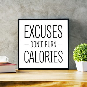 May include: Black and white motivational quote on a framed poster that reads "Excuses - Don't Burn - Calories". The poster is sitting on a wooden table with a white coffee cup and a book.