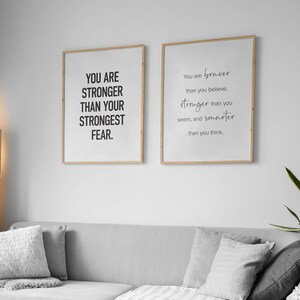 K&ouml;nnte beinhalten: Zwei gerahmte Motivationsposter mit wei&szlig;em Hintergrund und schwarzem Text. Das linke Poster sagt "You are stronger than your strongest fear." Das rechte Poster sagt "You are braver than you believe, stronger than you seem, and smarter than you think."