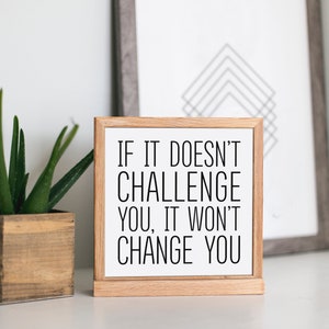 May include: A wooden sign with a white background and black text that reads "If it doesn't challenge you, it won't change you".