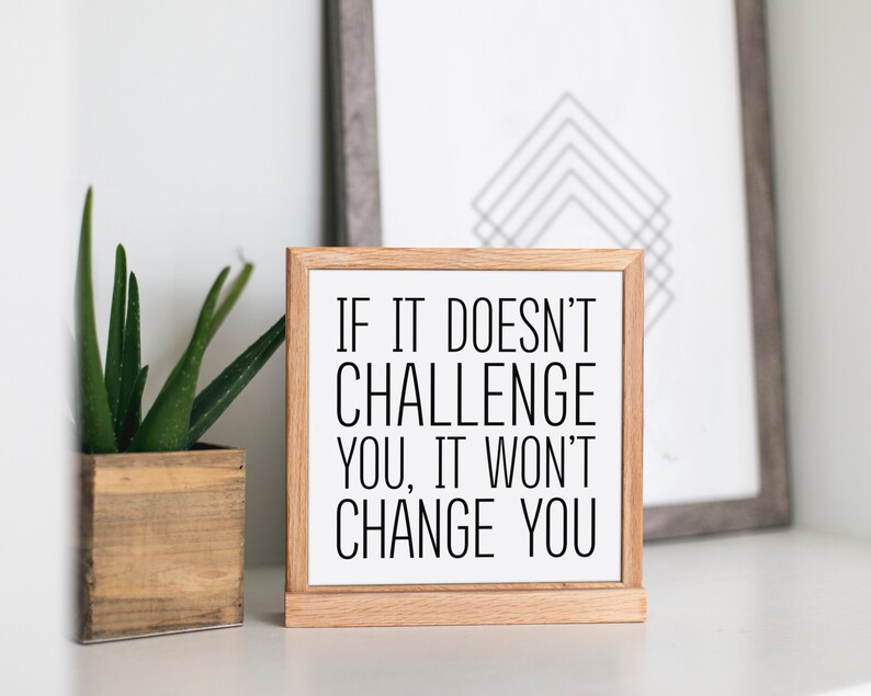 May include: A wooden sign with a white background and black text that reads "If it doesn't challenge you, it won't change you".