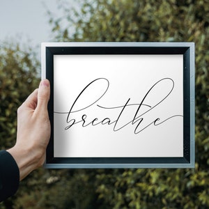 May include: A framed print with the word "breathe" written in a cursive font on a white background.