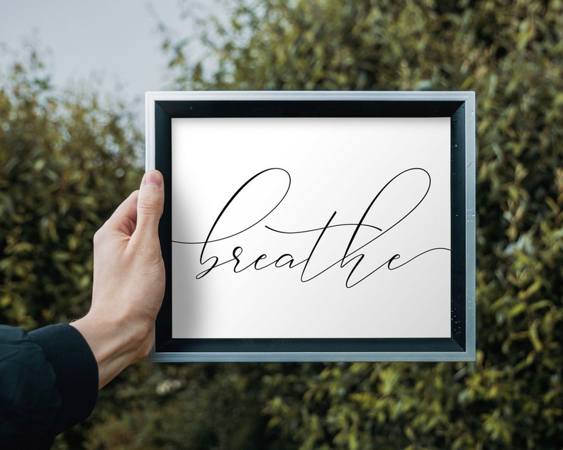 May include: A framed print with the word "breathe" written in a cursive font on a white background.