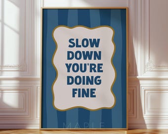 May include: A rectangular wall art print featuring a dark blue background with vertical stripes. In the center, a white scalloped-edge shape with a gold border contains the dark blue text: SLOW DOWN YOU'RE DOING FINE. The word MAPLE is at the bottom.