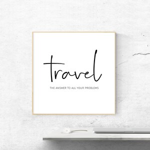 May include: A framed print with the word "travel" in black script, with the phrase "the answer to all your problems" below it. The print is in a light wood frame, set against a white wall.
