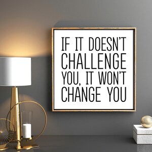 May include: A motivational quote in a black frame on a gray wall. The quote reads "If it doesn't challenge you, it won't change you."
