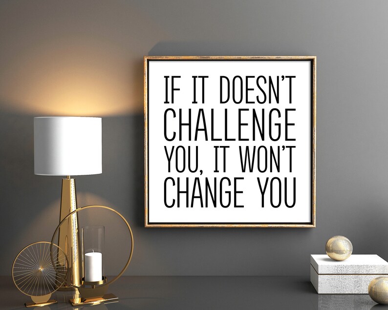 May include: A motivational quote in a black frame on a gray wall. The quote reads "If it doesn't challenge you, it won't change you."