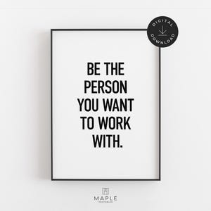 Op de afbeelding: Een ingelijste print met de tekst "BE THE PERSON YOU WANT TO WORK WITH" in vette zwarte letters. De print zit in een zwart frame en heeft een witte achtergrond. Een digitaal download-pictogram staat in de rechterbovenhoek.