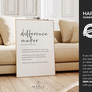 May include: A framed print with the words "difference maker" in black script. The definition of "difference maker" is listed below the title. The print is displayed in a living room setting.