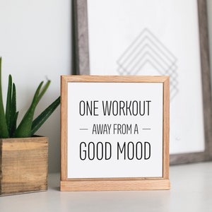 May include: A wooden framed sign with white background and black text that reads "ONE WORKOUT - AWAY FROM A - GOOD MOOD".