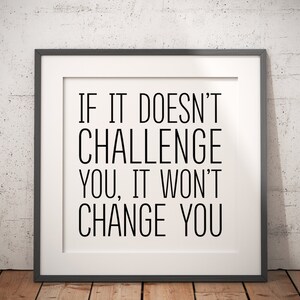 May include: A black and white motivational quote in a black frame against a white brick wall. The quote reads "If it doesn't challenge you, it won't change you."
