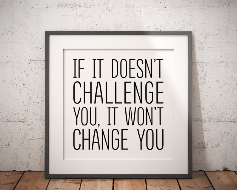 May include: A black and white motivational quote in a black frame against a white brick wall. The quote reads "If it doesn't challenge you, it won't change you."