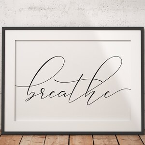 May include: A black framed print with a white background and the word "breathe" written in a cursive font.