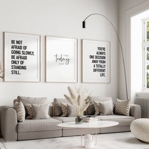 May include: Three framed inspirational quotes on a white wall above a gray couch with throw pillows. The quotes are: "Be not afraid of going slowly, be afraid only of standing still.", "Today make count", and "You're always one decision away from a totally different life."