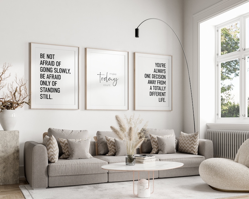 May include: Three framed inspirational quotes on a white wall above a gray couch with throw pillows. The quotes are: "Be not afraid of going slowly, be afraid only of standing still.", "Today make count", and "You're always one decision away from a totally different life."