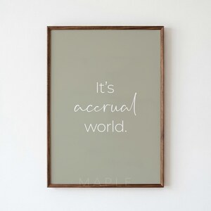 Può includere: Una stampa artistica da parete rettangolare in una cornice di legno scuro con sfondo verde salvia e il testo bianco It's accrual world. Il design utilizza una combinazione di un carattere sans-serif pulito e un corsivo delicato per la parola accrual.