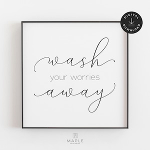 May include: A framed print with the words "wash your worries away" in elegant black script. The print is set against a white background and framed in a black border. A digital download icon is in the upper right corner.