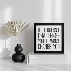 May include: Black framed motivational quote print with the text "If it doesn't challenge you, it won't change you." The print is sitting on a white shelf with a black vase and dried palm leaves.