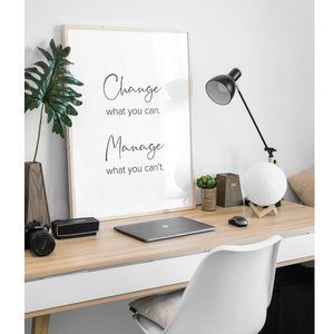 K&ouml;nnte beinhalten: Ein gerahmtes Motivationszitat auf wei&szlig;em Hintergrund mit schwarzem Text, der lautet "Change what you can. Manage what you can't." Der Rahmen befindet sich auf einem Schreibtisch mit einem Laptop, einer Lampe und einer Mondlampe.