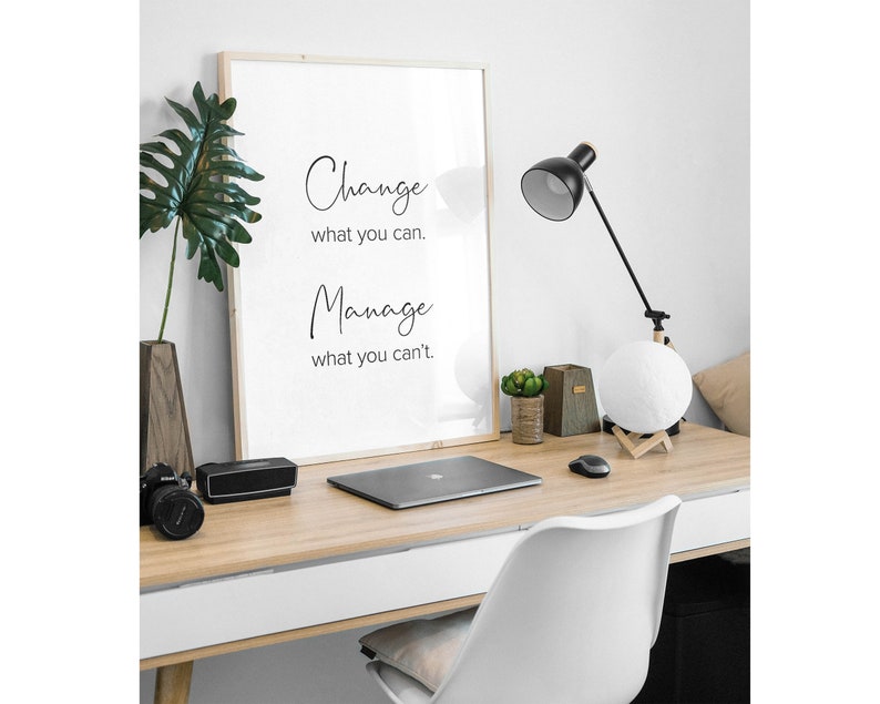 K&ouml;nnte beinhalten: Ein gerahmtes Motivationszitat auf wei&szlig;em Hintergrund mit schwarzem Text, der lautet "Change what you can. Manage what you can't." Der Rahmen befindet sich auf einem Schreibtisch mit einem Laptop, einer Lampe und einer Mondlampe.