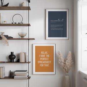 Puede incluir: Una estanter&iacute;a de pared con estantes de madera y soportes de metal negro. Se muestran dos impresiones enmarcadas: una azul marino con la palabra "accountant" y una definici&oacute;n, y otra naranja con el texto "Relax, I have the perfect spreadsheet for that."