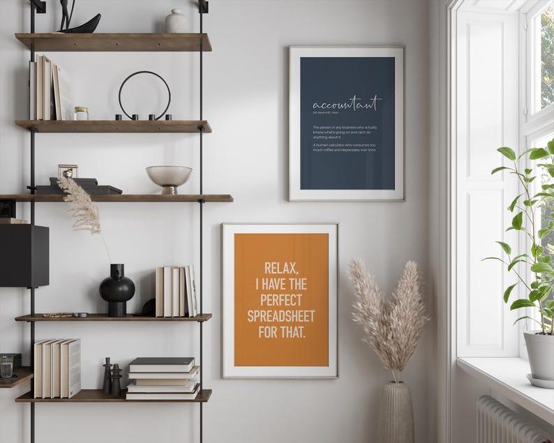 Puede incluir: Una estanter&iacute;a de pared con estantes de madera y soportes de metal negro. Se muestran dos impresiones enmarcadas: una azul marino con la palabra "accountant" y una definici&oacute;n, y otra naranja con el texto "Relax, I have the perfect spreadsheet for that."