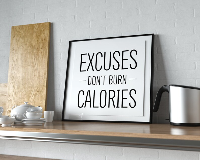 May include: A black framed motivational poster with white text that reads "Excuses - Don't Burn - Calories" on a white background. The poster is sitting on a wooden worktop.