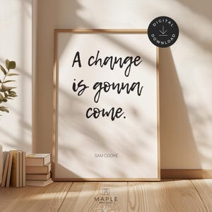 Può includere: Una stampa incorniciata con la frase "A change is gonna come" in stile scritto a mano, attribuita a Sam Cooke. La stampa è in una cornice di legno chiaro e include un badge "Download digitale".