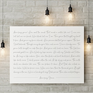 K&ouml;nnte beinhalten: Ein wei&szlig;er Leinwanddruck mit schwarzem Text, der die Worte des Kirchenliedes "Amazing Grace" zeigt. Der Text ist mittig auf der Leinwand platziert und von einem wei&szlig;en Rand umgeben.