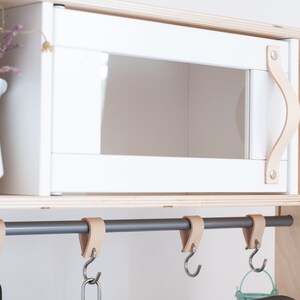 May include: White wooden cabinet with a leather handle and a gray metal rod with leather hooks hanging from it.