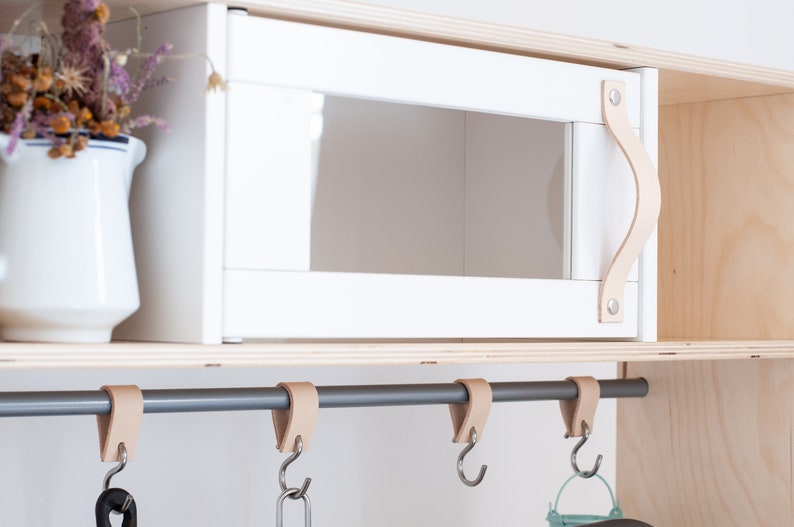 May include: White wooden cabinet with a leather handle and a gray metal rod with leather hooks hanging from it.