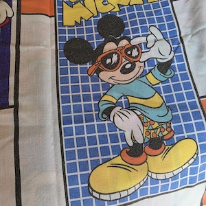 May include: A fabric print featuring Mickey Mouse wearing orange sunglasses, a blue and yellow shirt, and patterned shorts. The character stands against a blue grid background with the text Cool Mickey in yellow. The Walt Disney Co. text is at the bottom.