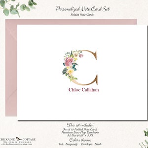 May include: Personalized note card set with a floral monogram of the letter C in gold with pink and yellow flowers. The name Chloe Callahan is printed below the monogram. The set includes 10 folded note cards and envelopes. The ink color is burgundy and the envelope color is blush.