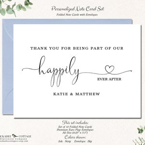 May include: A personalized note card set with a white card and a light blue envelope. The card reads "THANK YOU FOR BEING PART OF OUR happily EVER AFTER" with the names KATIE & MATTHEW. A silver pen rests on the right.