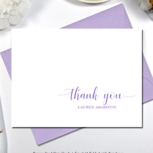 May include: White note card with a lavender "thank you" script and the name "LAUREN ADAMSON". The card is on a lavender envelope. A white pen and a decorative flower are in the background. The text reads "Personalized Note Cards".