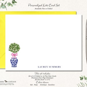 May include: A set of personalized note cards featuring a watercolor illustration of a potted topiary with a pink ribbon. The cards are available in folded or flat styles and come with envelopes. The text on the card reads "LAUREN SUMMERS" and includes details about the set, such as the size and colors. The text also says "This set includes: Set of 10 Folded or 12 Flat Note Cards Premium Euro Flap Envelopes A2 Size (4.25" x 5.5") Colors shown: Ink: Navy Envelope: Sunshine"