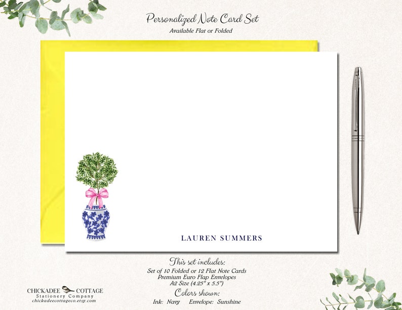 May include: A set of personalized note cards featuring a watercolor illustration of a potted topiary with a pink ribbon. The cards are available in folded or flat styles and come with envelopes. The text on the card reads "LAUREN SUMMERS" and includes details about the set, such as the size and colors. The text also says "This set includes: Set of 10 Folded or 12 Flat Note Cards Premium Euro Flap Envelopes A2 Size (4.25" x 5.5") Colors shown: Ink: Navy Envelope: Sunshine"