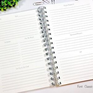 May include: An open spiral bound journal with lined pages for writing down prayers, gratitude, scripture, and thoughts. The journal has the words "Prayer Requests", "Gratitude", "Scripture", "On My Heart", "Let Go & Let God", and "Answered Prayers" printed on the pages.