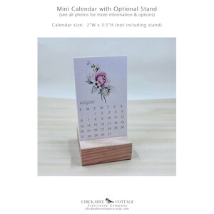 K&ouml;nnte beinhalten: Ein kleiner, wei&szlig;er Kalender mit einem Aquarell-Blumendesign mit einer rosa Rose. Der Kalender ist f&uuml;r August und wird auf einem Holzst&auml;nder pr&auml;sentiert. Der Kalender misst 5 cm breit und 9 cm hoch.