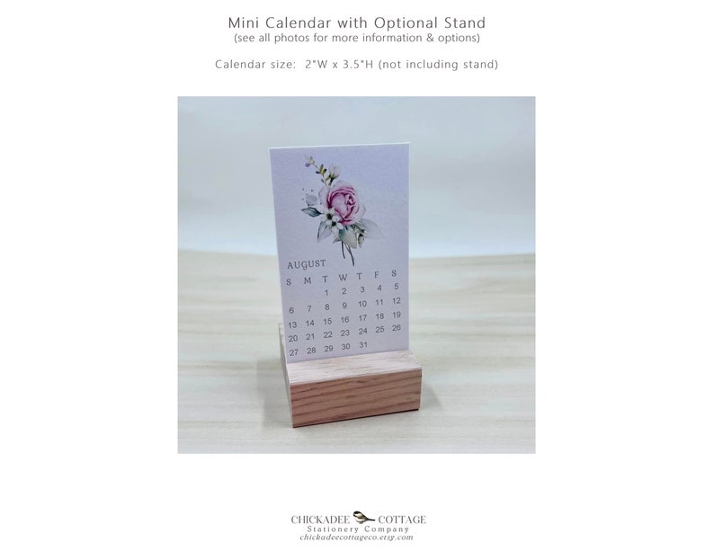 K&ouml;nnte beinhalten: Ein kleiner, wei&szlig;er Kalender mit einem Aquarell-Blumendesign mit einer rosa Rose. Der Kalender ist f&uuml;r August und wird auf einem Holzst&auml;nder pr&auml;sentiert. Der Kalender misst 5 cm breit und 9 cm hoch.