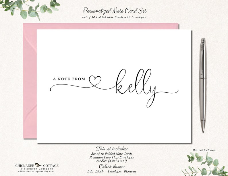 May include: A personalized note card set with a pink envelope. The white card features the text "A NOTE FROM" and the name "kelly" in elegant black script. A silver pen rests beside the card. The set includes 10 folded note cards.