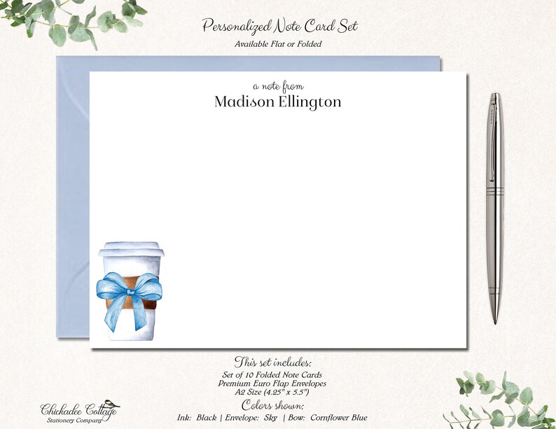 May include: Personalized note card set featuring a watercolour illustration of a coffee cup with a blue ribbon. The set includes 10 folded note cards and envelopes. The card size is 10.8 cm by 14 cm. The ink colour is black, the envelope colour is sky blue, and the bow colour is cornflower blue.