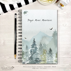 May include: Personalized prayer journal with a watercolor illustration of a mountain range, trees, and a moon. The text "Prayer Moves Mountains" is at the top of the journal, and the text "Adam Williams" is at the bottom. The journal is 5.5 inches by 8.5 inches and has a black coil.