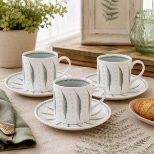 May include: Three white ceramic teacups and matching saucers decorated with a repeating sage green fern leaf pattern and small dots. The cups feature a sage green interior rim, and the saucers display a radiating fern leaf design.