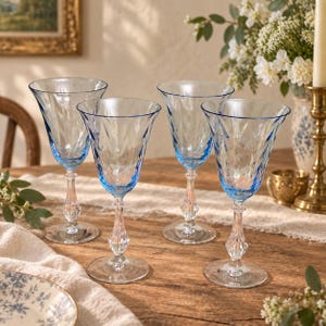 May include: A set of four stemmed wine glasses featuring light blue tinted bowls with a textured, rippled surface pattern. Each glass has a clear, faceted stem and a circular base, arranged on a wooden surface for a clear view of the design.