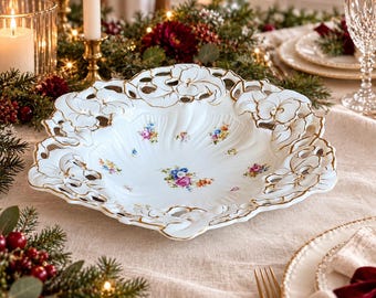 Puede incluir: Un cuenco de porcelana blanca con un borde calado y festoneado con detalles dorados. El centro y los laterales están decorados con pequeños ramos de flores coloridas, incluyendo rosas, azules y amarillos sobre una superficie blanca estriada.