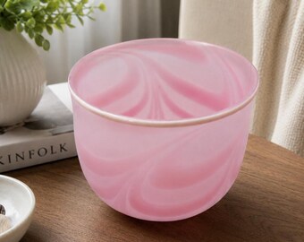 May include: A translucent glass bowl featuring a swirling pattern of soft pink and white colors. The bowl has a smooth, rounded shape with a consistent rim and a polished finish, showcasing a marbled aesthetic throughout the entire exterior surface.