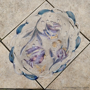 May include: A clear glass serving bowl with a scalloped edge and an etched design of purple and gold fish and seashells.