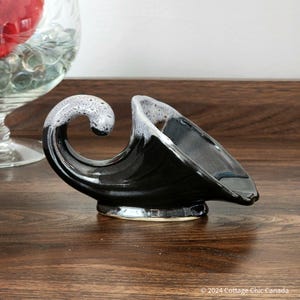 Könnte beinhalten: Eine schwarze dekorative Keramikschale mit einem einzigartigen wellenförmigen Design. Die Schale hat einen geschwungenen, scrollartigen Griff mit einer gesprenkelten weiß-grauen Oberfläche. Der Innenraum ist glatt und glänzend, perfekt für kleine Gegenstände.