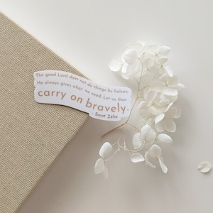 Puede incluir: Una pegatina blanca con una cita de Santa Zelia: "El buen Señor no hace las cosas a medias; siempre da lo que necesitamos. Sigamos adelante con valentía."